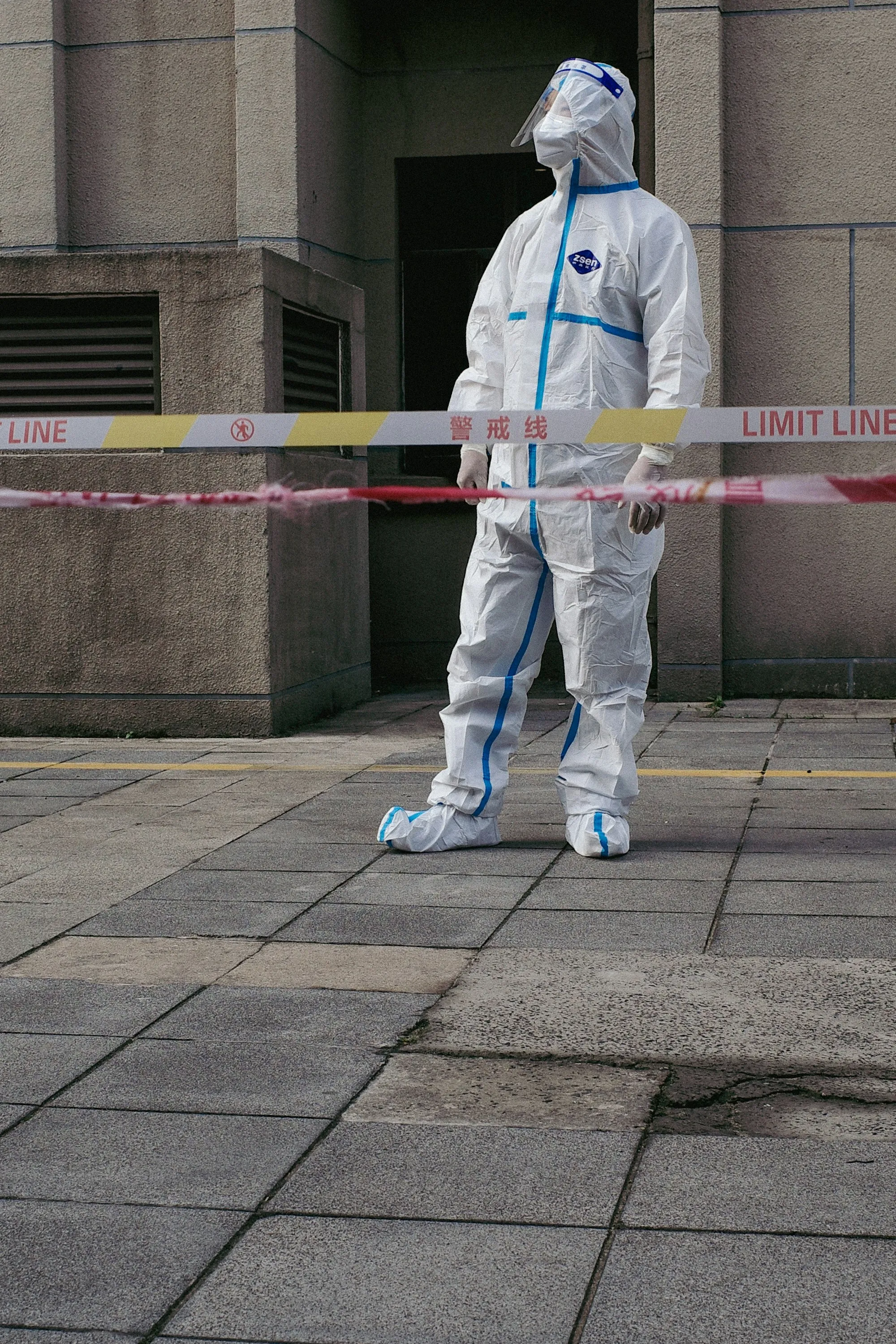 Worker in a protective suit and boot covers behind barrier tape